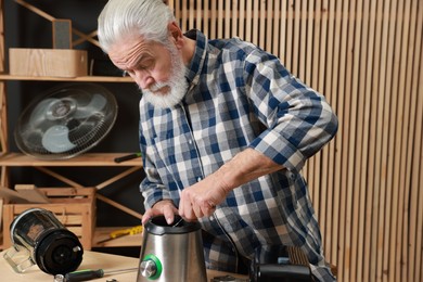 Photo of Relaxing hobby. Senior man repairing blender with wrench in workshop