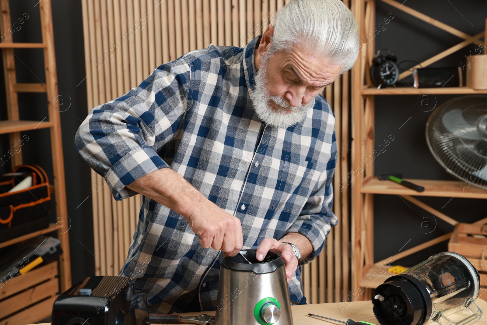 Photo of Relaxing hobby. Senior man repairing blender with wrench in workshop