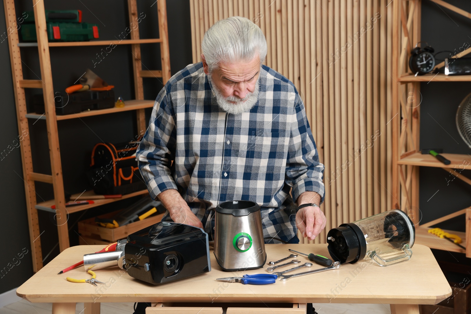 Photo of Relaxing hobby. Senior man repairing blender and meat grinder in workshop