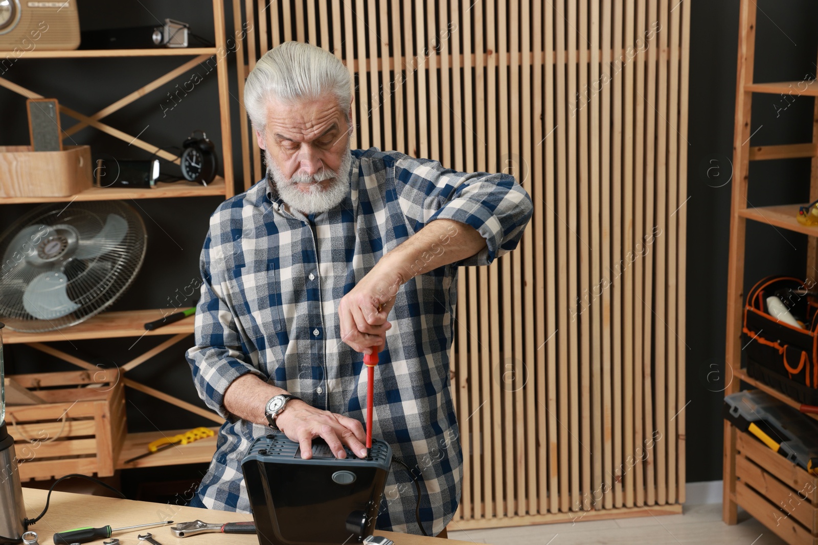 Photo of Relaxing hobby. Senior man repairing meat grinder with screwdriver in workshop