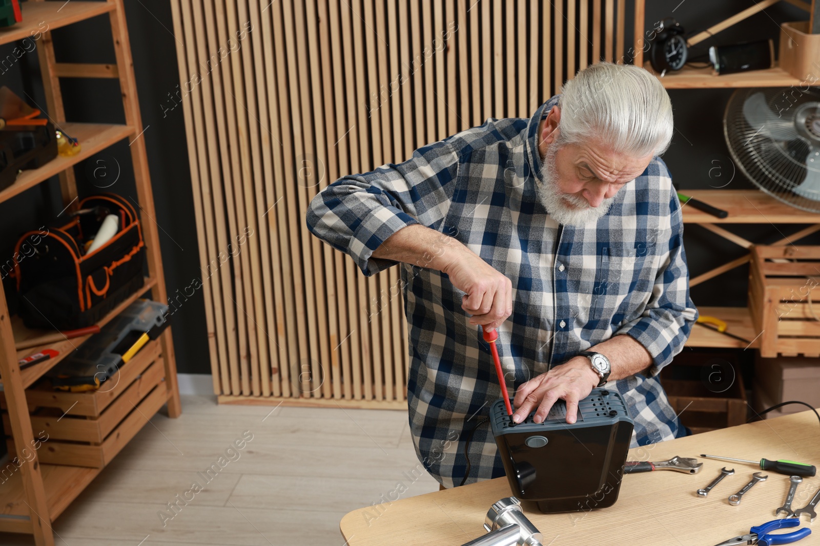 Photo of Relaxing hobby. Senior man repairing meat grinder with screwdriver in workshop