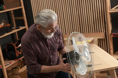 Photo of Relaxing hobby. Senior man repairing fan in workshop