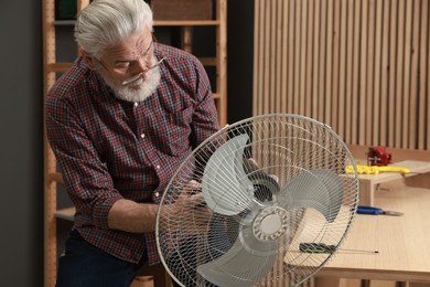 Photo of Relaxing hobby. Senior man repairing fan in workshop