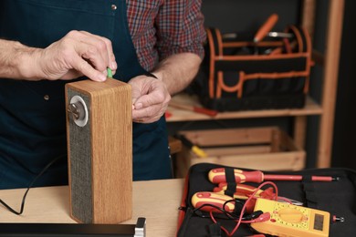 Photo of Relaxing hobby. Senior man testing portable bluetooth speaker in workshop, closeup