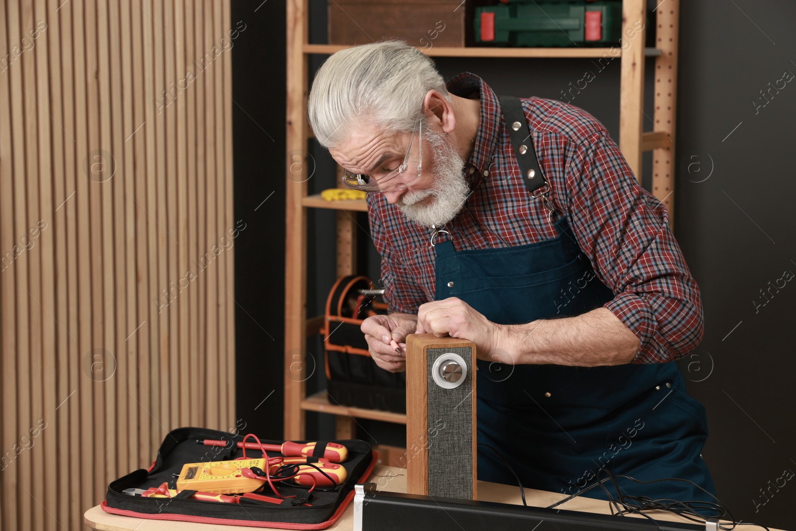 Photo of Relaxing hobby. Senior man testing portable bluetooth speaker in workshop