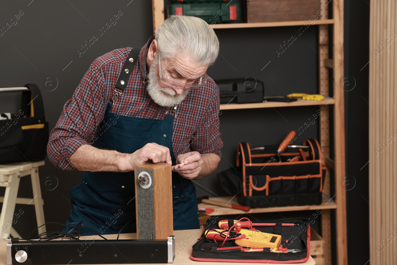 Photo of Relaxing hobby. Senior man testing portable bluetooth speaker in workshop