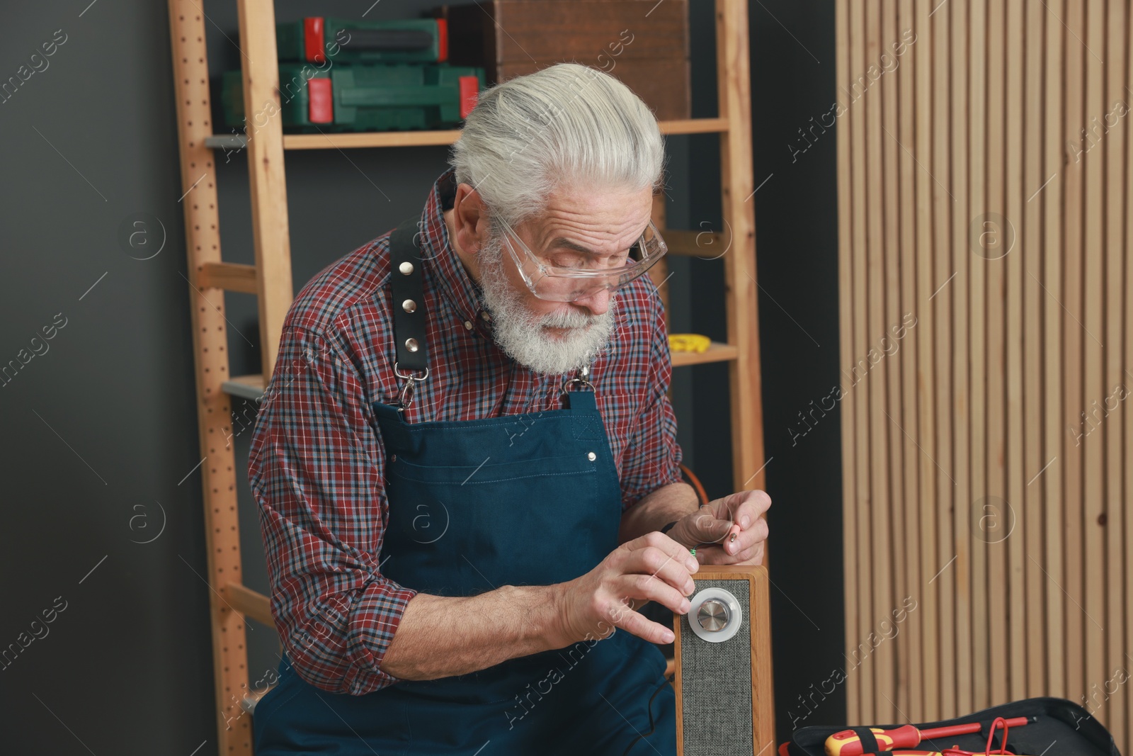 Photo of Relaxing hobby. Senior man testing portable bluetooth speaker in workshop