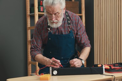 Photo of Relaxing hobby. Senior man testing soundbar with multimeter in workshop