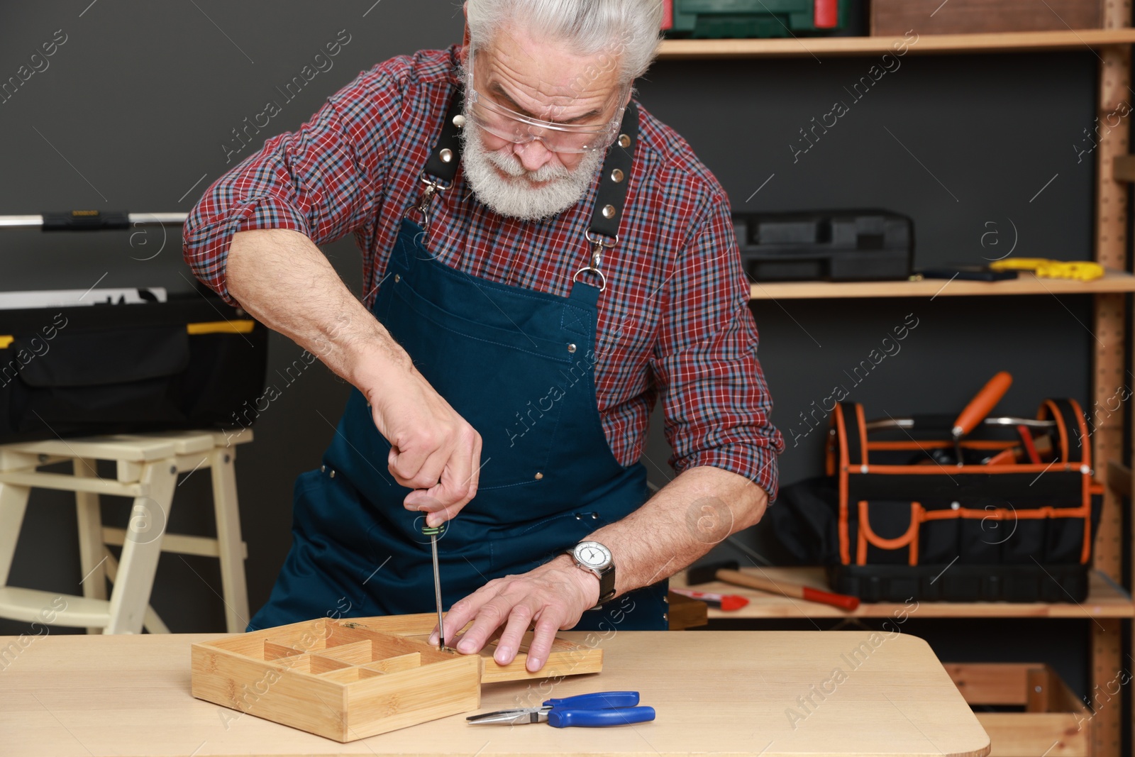 Photo of Relaxing hobby. Senior man repairing wooden jewelry box with screwdriver in workshop