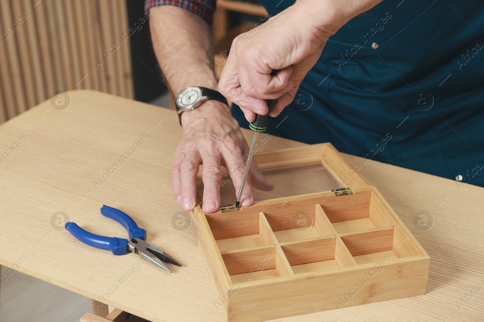 Photo of Relaxing hobby. Senior man repairing wooden jewelry box with screwdriver in workshop, closeup