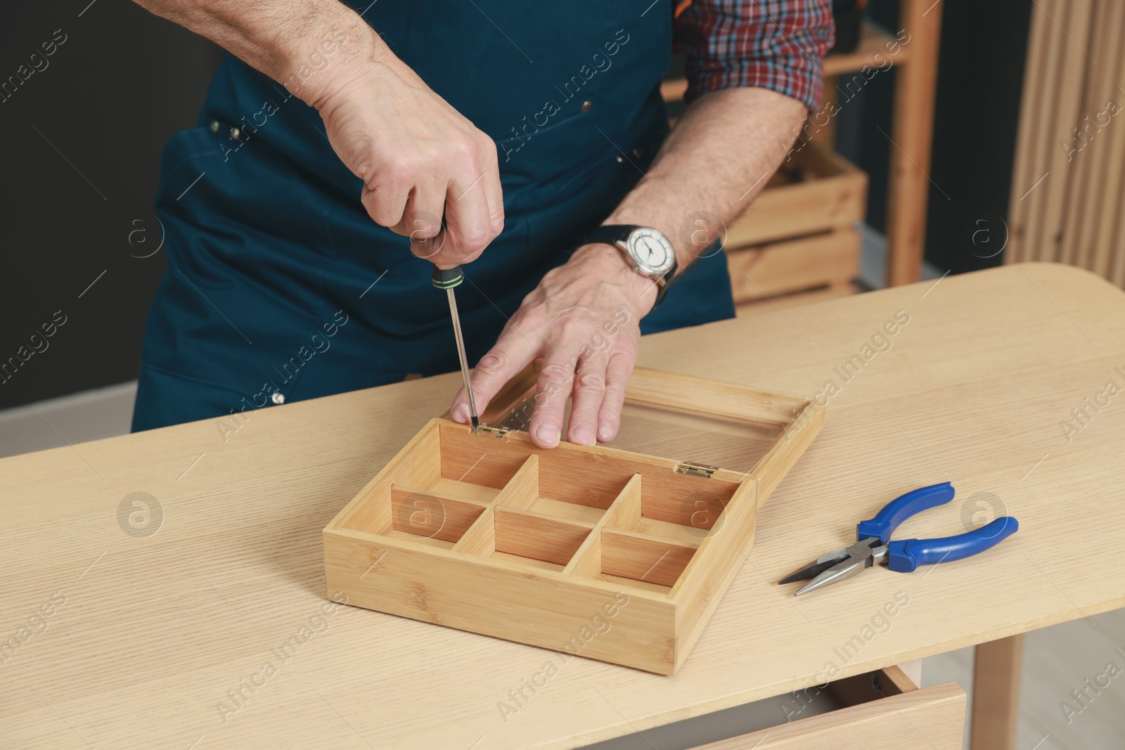 Photo of Relaxing hobby. Senior man repairing wooden jewelry box with screwdriver in workshop, closeup