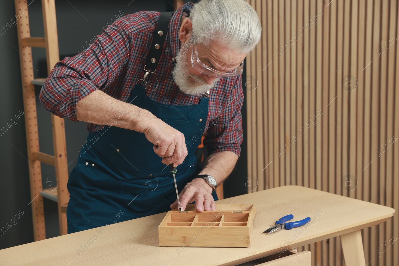 Photo of Relaxing hobby. Senior man repairing wooden jewelry box with screwdriver in workshop