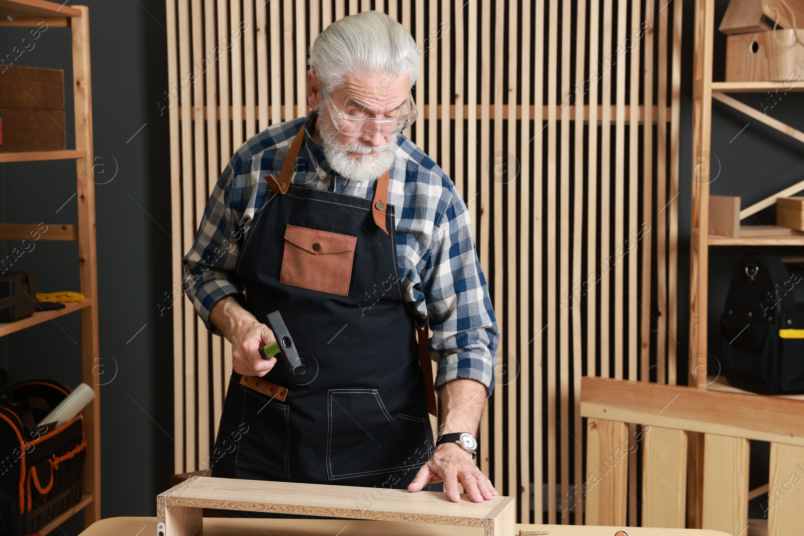 Photo of Relaxing hobby. Senior man working with wooden shelf and hammer in workshop