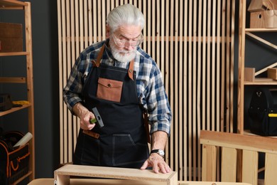 Photo of Relaxing hobby. Senior man working with wooden shelf and hammer in workshop