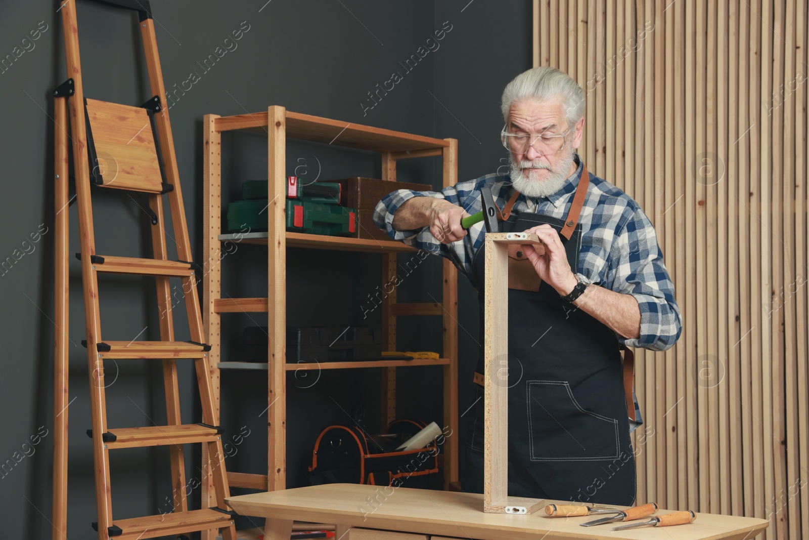 Photo of Relaxing hobby. Senior man repairing wooden shelf with hammer in workshop