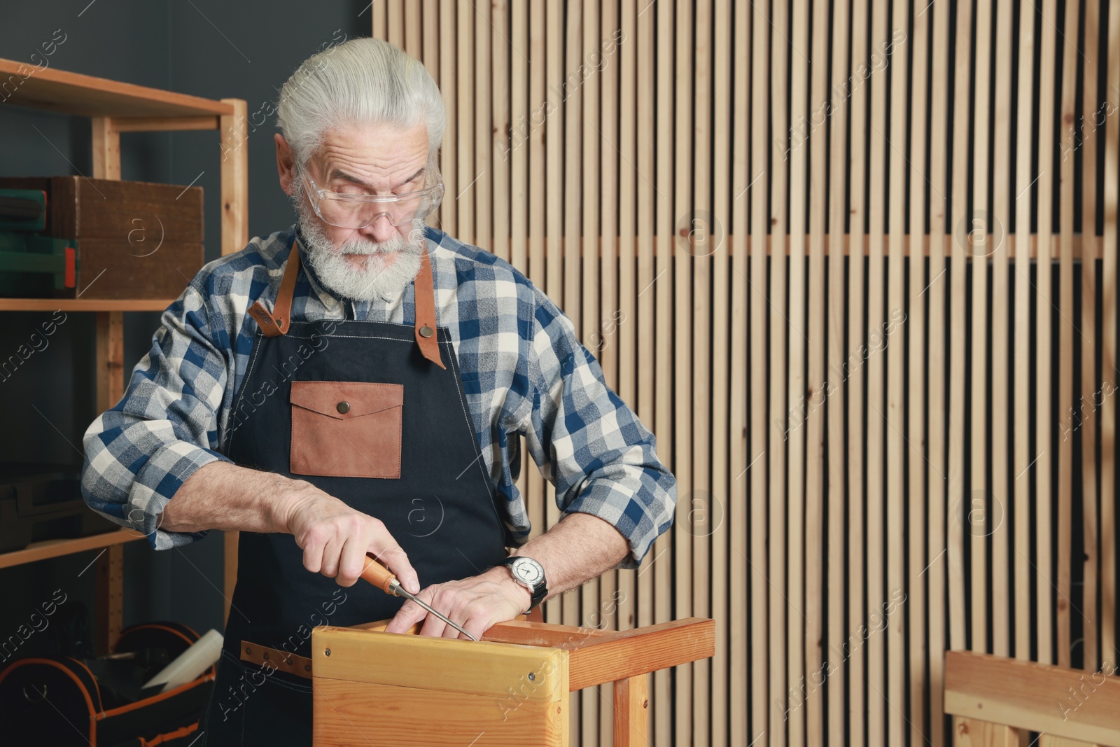 Photo of Relaxing hobby. Senior man repairing wooden stool with chisel in workshop