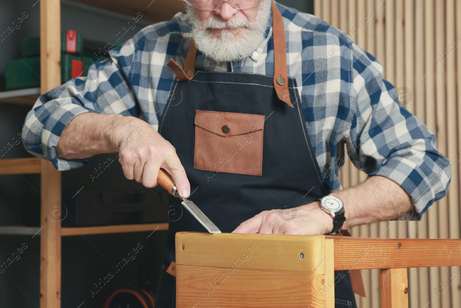 Photo of Relaxing hobby. Senior man repairing wooden stool with chisel in workshop, closeup