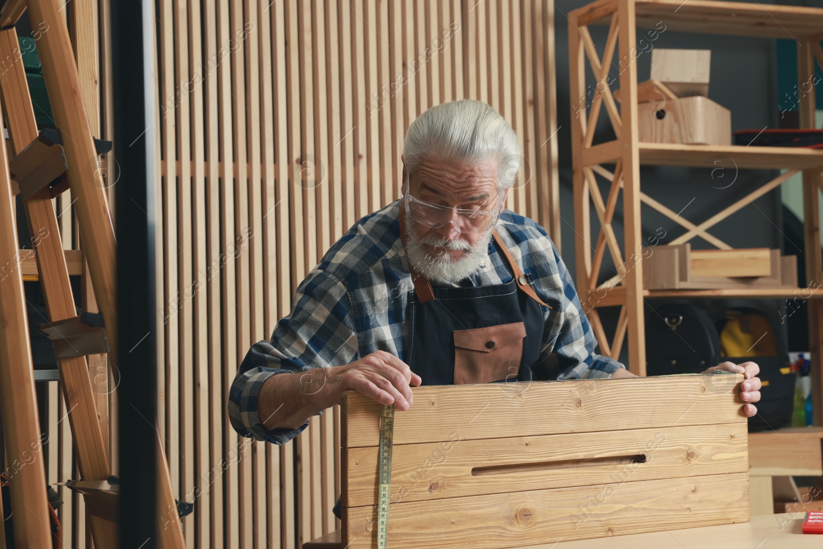 Photo of Relaxing hobby. Senior man measuring wooden plank with tape in workshop