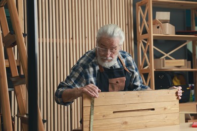 Photo of Relaxing hobby. Senior man measuring wooden plank with tape in workshop