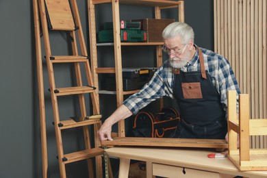 Photo of Relaxing hobby. Senior man measuring wooden plank with tape in workshop