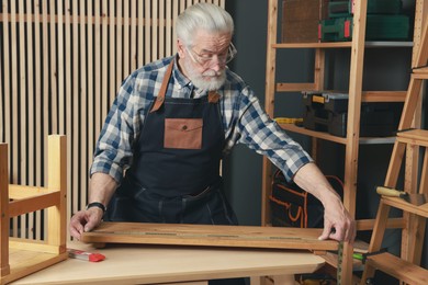 Photo of Relaxing hobby. Senior man measuring wooden plank with tape in workshop