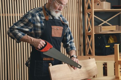 Photo of Relaxing hobby. Senior man working with wooden plank and saw in workshop