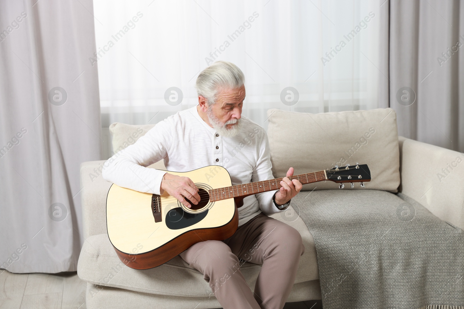 Photo of Relaxing hobby. Senior man playing guitar on sofa at home