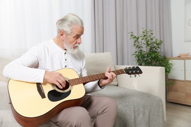 Photo of Relaxing hobby. Senior man playing guitar on sofa at home