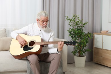 Relaxing hobby. Senior man playing guitar on sofa at home