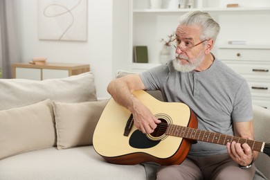 Photo of Relaxing hobby. Senior man playing guitar on sofa at home