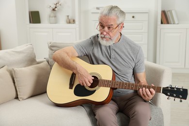 Photo of Relaxing hobby. Senior man playing guitar on sofa at home