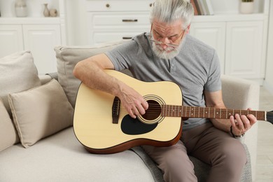 Photo of Relaxing hobby. Senior man playing guitar on sofa at home