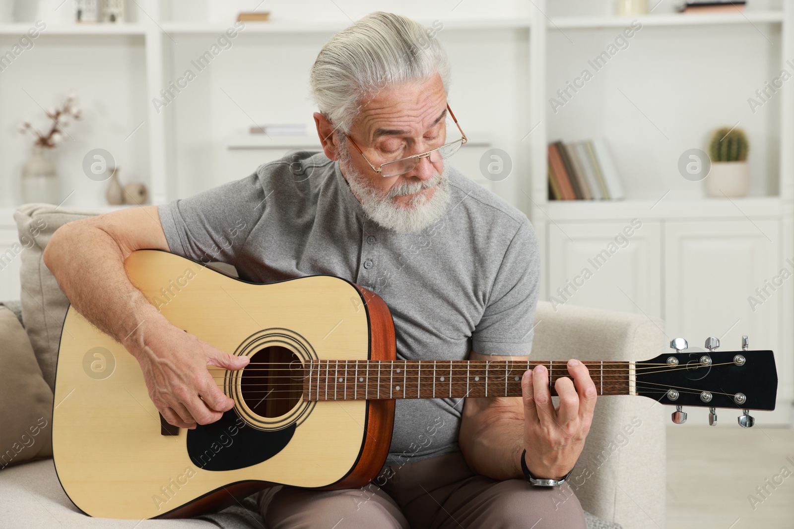 Photo of Relaxing hobby. Senior man playing guitar on sofa at home