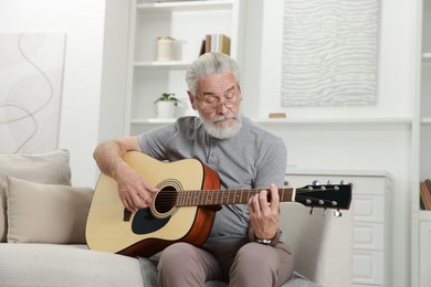 Photo of Relaxing hobby. Senior man playing guitar on sofa at home