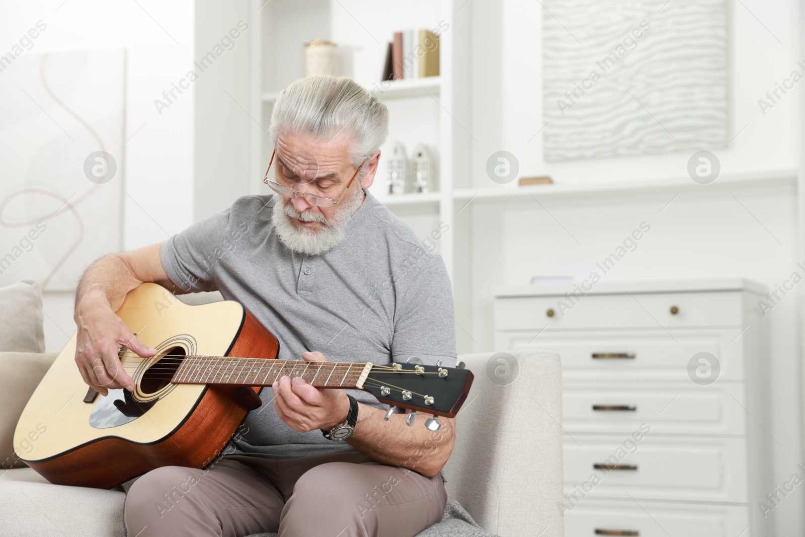 Photo of Relaxing hobby. Senior man playing guitar on sofa at home