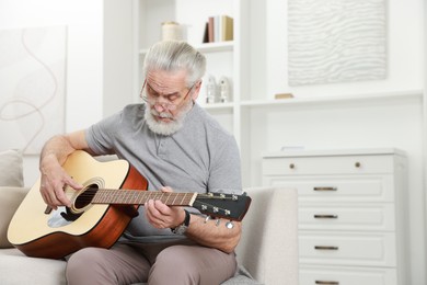 Relaxing hobby. Senior man playing guitar on sofa at home