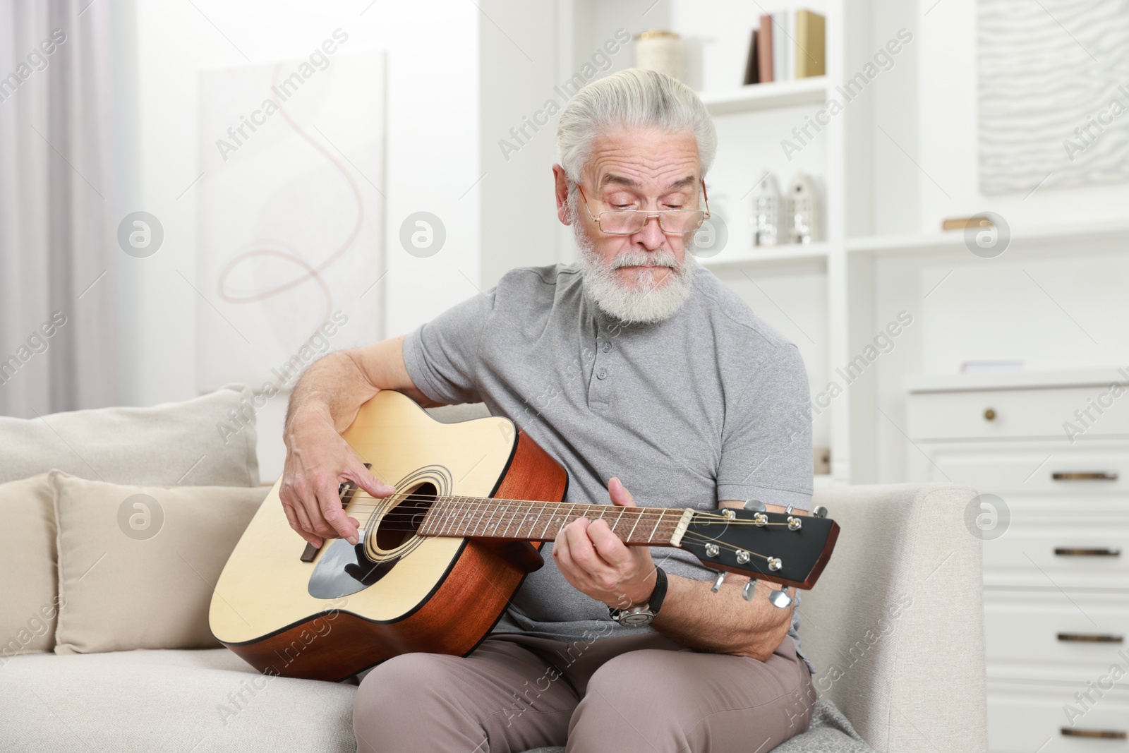 Photo of Relaxing hobby. Senior man playing guitar on sofa at home