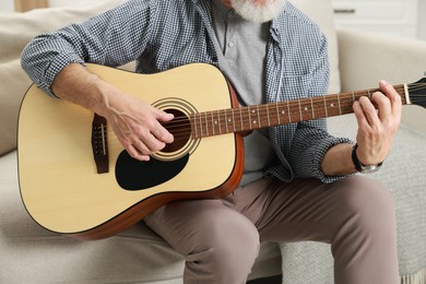 Photo of Relaxing hobby. Senior man playing guitar on sofa at home, closeup