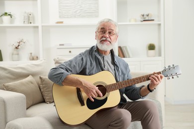 Photo of Relaxing hobby. Senior man playing guitar on sofa at home