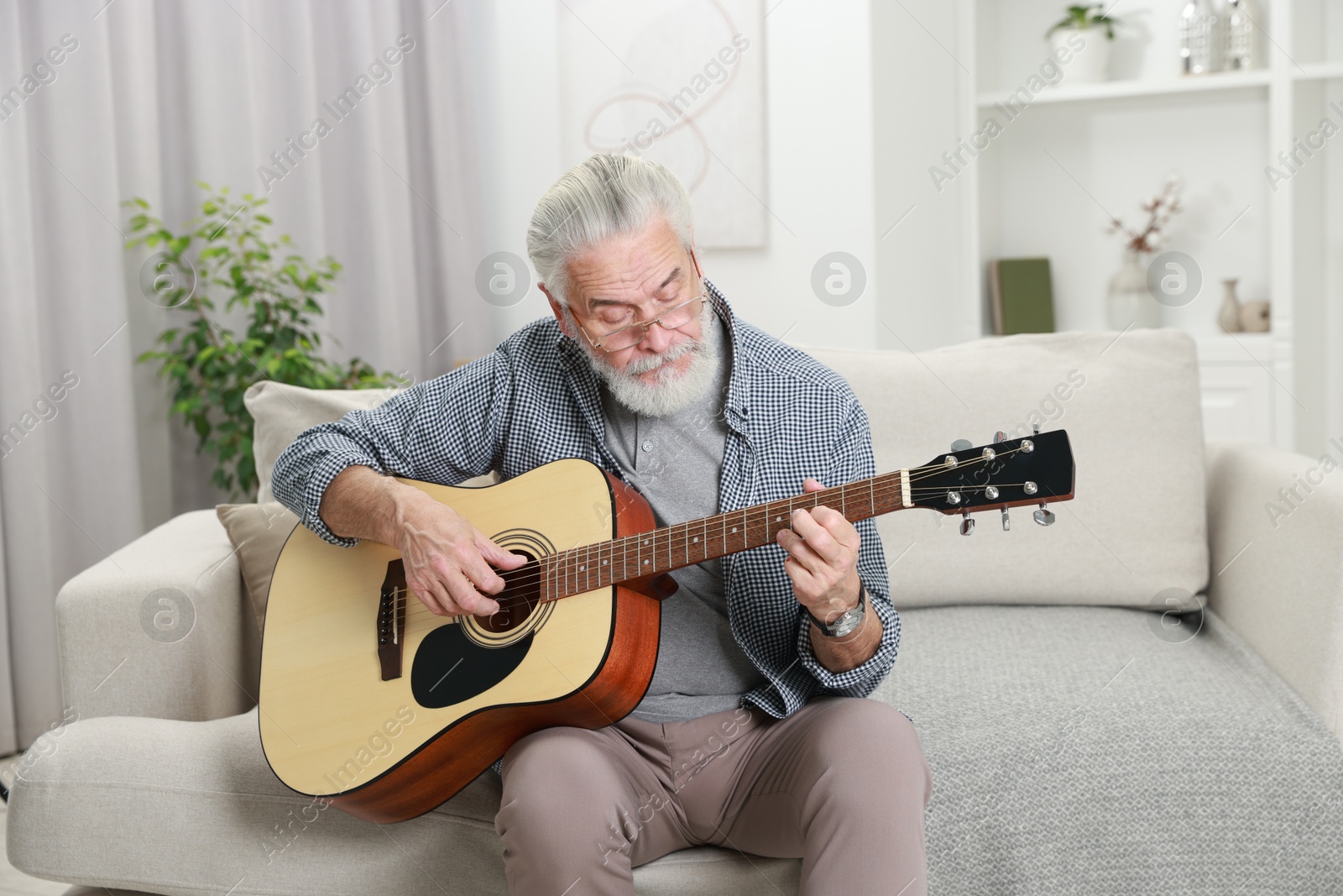 Photo of Relaxing hobby. Senior man playing guitar on sofa at home