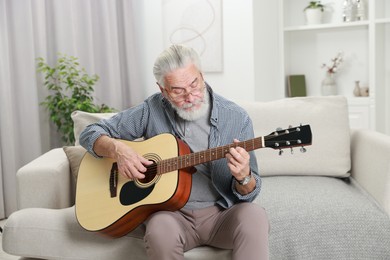 Photo of Relaxing hobby. Senior man playing guitar on sofa at home