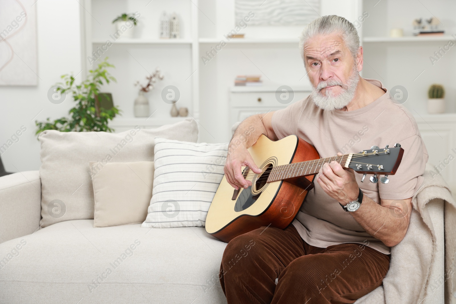 Photo of Relaxing hobby. Senior man playing guitar on sofa at home