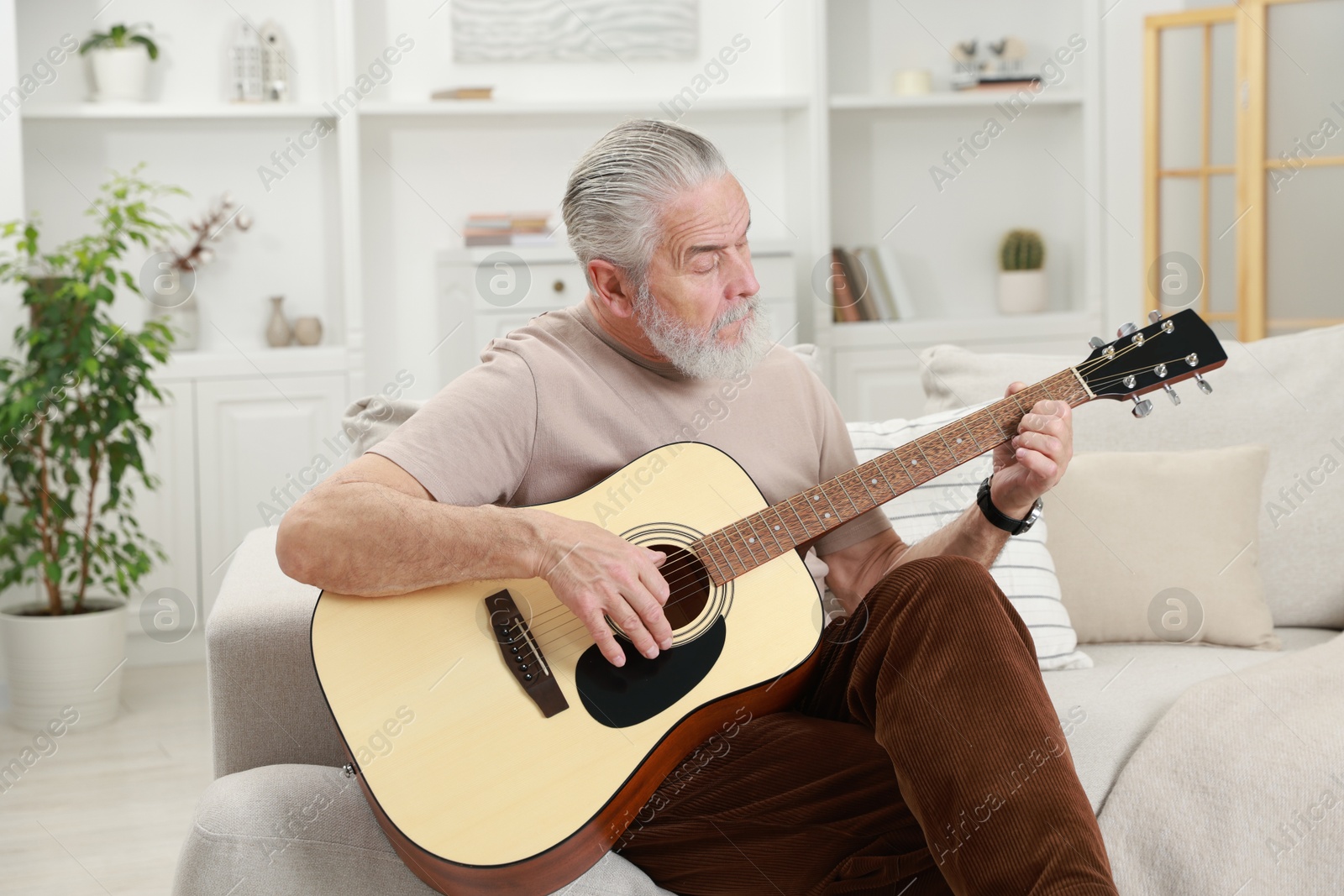 Photo of Relaxing hobby. Senior man playing guitar on sofa at home