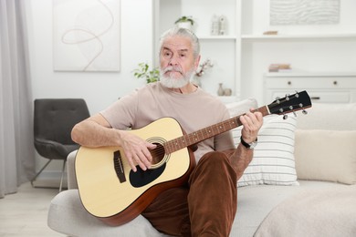 Photo of Relaxing hobby. Senior man playing guitar on sofa at home