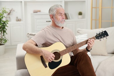 Photo of Relaxing hobby. Senior man playing guitar on sofa at home