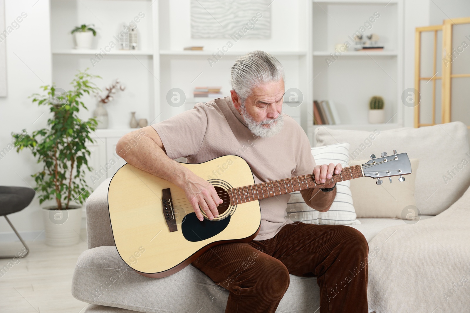 Photo of Relaxing hobby. Senior man playing guitar on sofa at home