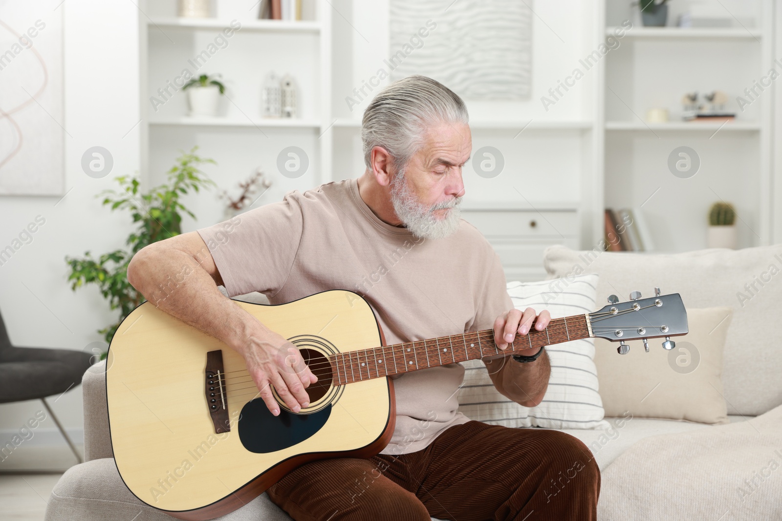 Photo of Relaxing hobby. Senior man playing guitar on sofa at home