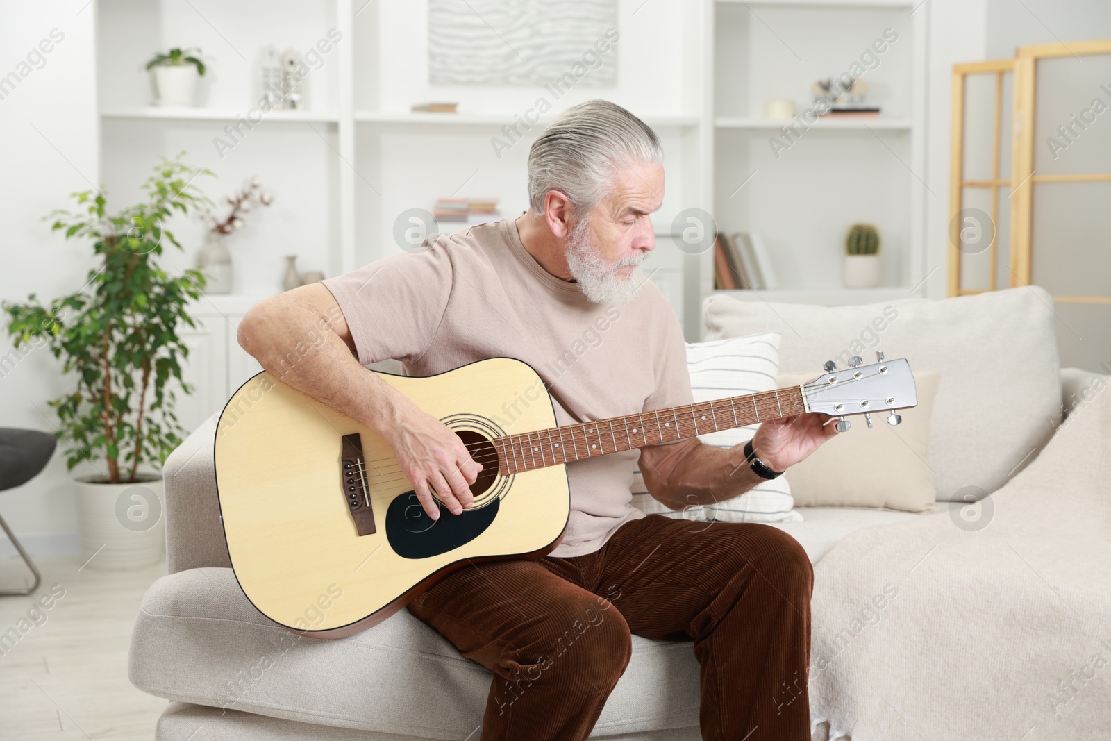 Photo of Relaxing hobby. Senior man playing guitar on sofa at home