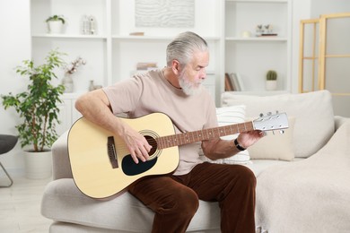 Relaxing hobby. Senior man playing guitar on sofa at home