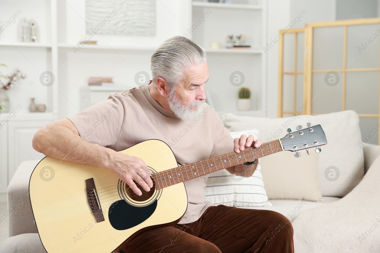 Photo of Relaxing hobby. Senior man playing guitar on sofa at home